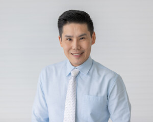 Portrait close up shot of asian male model with short black hair wearing light blue shirt with white dot necktie stand smiling in front of white background