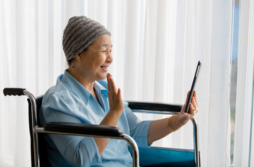 Older Asian woman patient covered the head with clothes effect from chemo treatment in cancer cure process waving hand to greeting family members