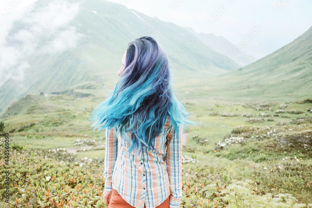 Wall mural Young woman waving her beautiful blue hair on a walk in the mountains.