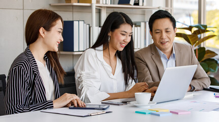 Fototapeta premium group of Asian businesspeople working communicating and looking at laptop screen while sitting on a desk together. Concentration brainstorming with good teamwork