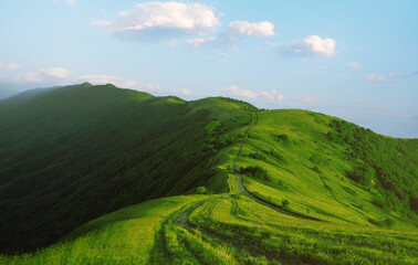 Landscape of blue sky and hills with meadows covered with green grass on a summer day.