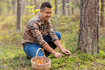 picking season and leisure people concept - happy smiling middle aged man with wicker basket of mushrooms in autumn forest
