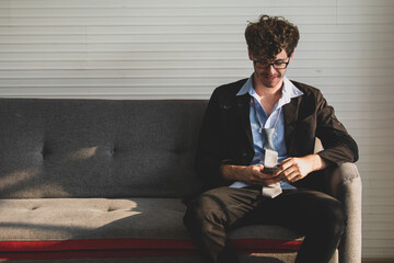 handsome caucasian businessman wearing black suit with loosen necktie sitting on a couch looking at a smartphone and raise fist happily. Success, employment concept