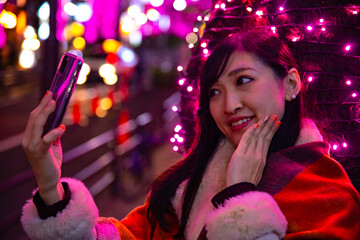 A Japanese girl shooting selfie at night illuminated street in Shibuya close shot