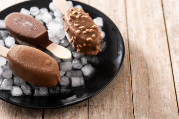 Chocolate popsicles and crushed ice on black plate on wooden table