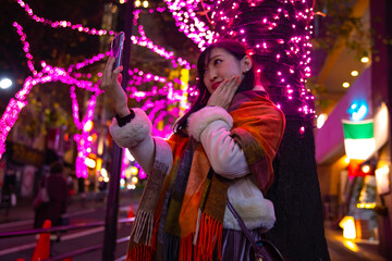 A Japanese girl shooting selfie at night illuminated street in Shibuya