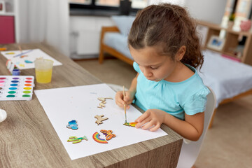 childhood, hobby and leisure concept - little girl with brush painting wooden chipboard items at home