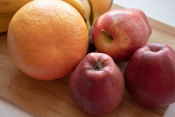 a set of fruits, red apples, a bunch of bananas and an orange, lie on a wooden board, on a light surface. Natural fruit dessert. A tasty, healthy snack, a slice of summer, a harvest. 