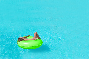 Fototapeta na wymiar Girl relaxing in a giant rubber ring in a large swimming pool with copy space, blue water and summer background