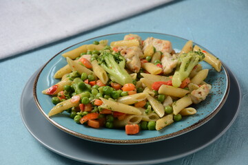 Pasta salad with baked vegetables and fried pieces of chicken breast . Penne pasta with broccoli, beans and carrots.