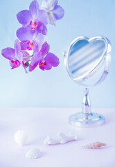mirror in the shape of a heart with a delicate orchid. still life with a mirror, a flower and shells on the table. makeup mirror and flowers