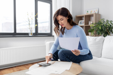 accounting, taxes and finances concept - young woman with papers and calculator at home