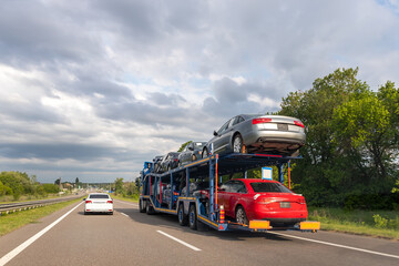 Tow truck car carrier semi trailer on highway carrying batch of damaged cars sold on insurance car...