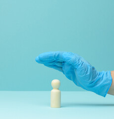 hand in a blue medical latex glove over a wooden figurine of a man