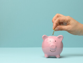 ceramic pink piggy bank and hand throwing a coin inside, finance savings concept