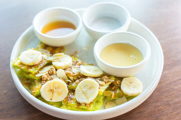 The Roti with sliced banana was served with sweetened condensed milk sugar and banana sauce , on top with sliced almond  put on white plate.