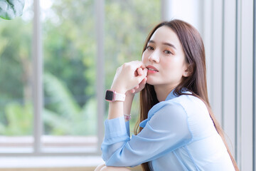 Asian beautiful woman wears blue shirt and smart watch and sits near window as background..