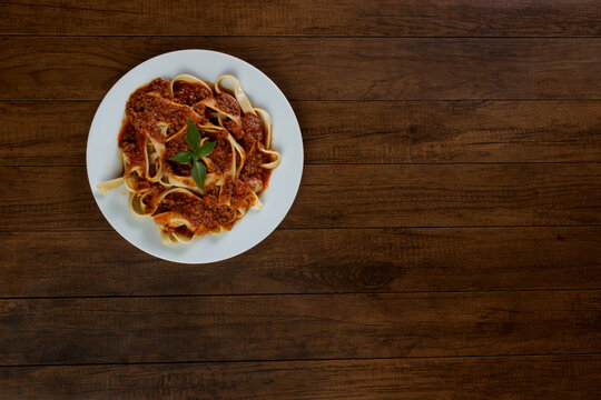 Pasta Tagliatelle with bolognese sauce and basil leaves served on a white plate. Food aligned at the top left of the photo with space for texts. Top shot.