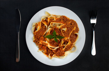 Pasta with bolognese sauce and finished with basil leaves served on the plate. Fork on the right...