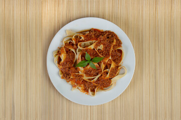 Pasta with bolognese sauce and basil leaves. Pasta served on the plate with light background. Top view photo with free spaces for texts.