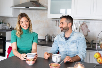 Happy couple chatting during breakfast.
Newlyweds talk while drinking coffee sitting at the kitchen table.
Smiles, lifestyle and happy morning.