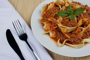 Pasta with bolognese sauce and basil leaves. Fork and knife on white napkin on the left. Gourmet close-up photo of typical popular pasta from Italy.