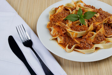 Tasty Pasta with bolognese sauce and basil leaves. Fork and knife on white napkin. Photo with space for text.