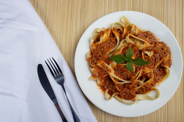 Pasta with bolognese sauce and basil leaves. Fork and knife on white napkin. Top photo with ample spaces for text on the left.