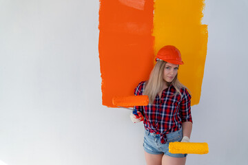 renovation of the premises. a girl painter in an orange construction helmet and gloves stands with two paint rollers in her hands