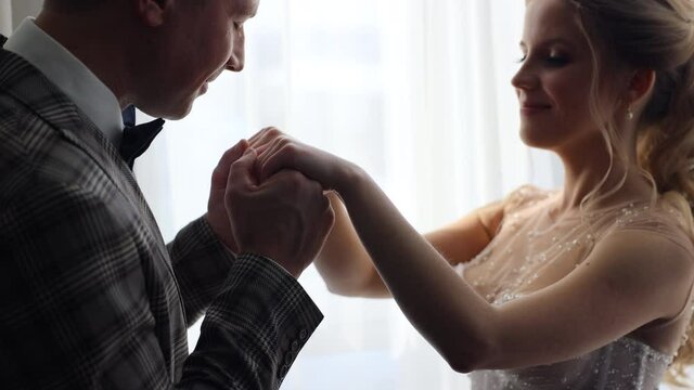 the groom in a three-piece suit approaches the bride in a white wedding dress and kisses her hands. The first meeting of the couple on the wedding day. Bride and wedding morning concept.