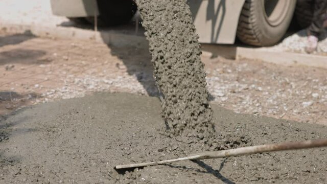 Workers are spreading the concrete that flows and pouring from a cement mixer truck, pouring liquid concrete into the roadway at the construction site.