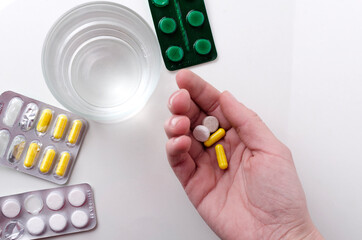 Top view of blisters pills, glass of water and woman hand who holding dose of pills