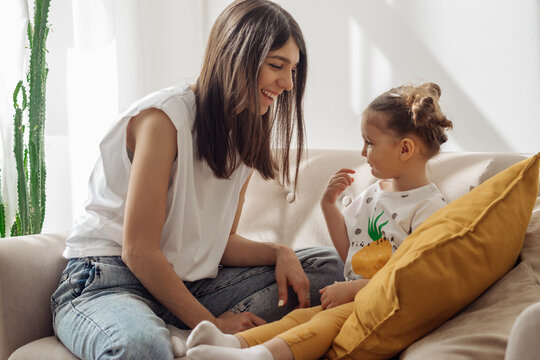 A dark-haired young mixed-race woman plays on the couch with her little daughter.Home interior design with houseplants.Time together.Family concept and Mother's Day concept.