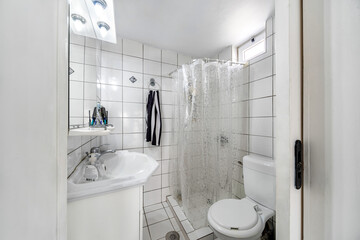Standard bathroom, with white sink, toilet, shower with curtain. White tiles. Selective focus