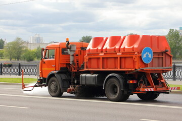 New Russian orange watering machine truck pours asphalt road, street washing in Moscow, city improvement by municipal services on a sunny summer day