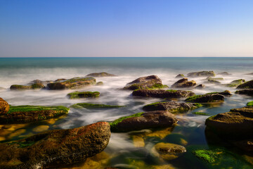 Fototapeta na wymiar Long exposure by the sea. Waves break against stones. 