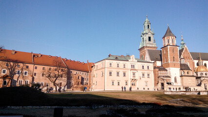 Fototapeta na wymiar Entrance to the castle. Couple walking on the street. Scenic view of the old town country on a sunny day. Beautiful scape with medieval castle. Group of young people sightseeing famous Krakow landmark