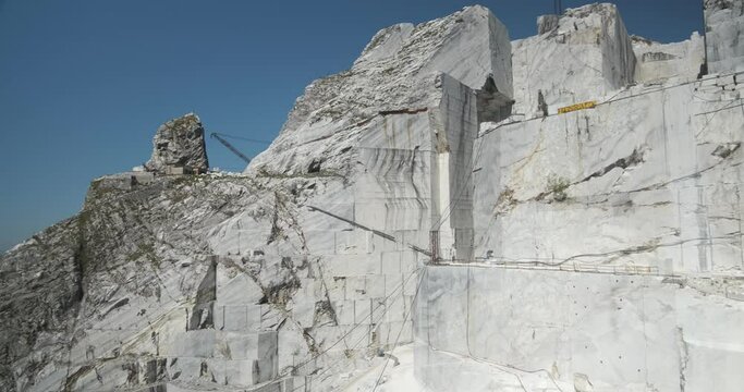 Large white marble quarry with blue sky background.There is a derrick type crane used to lift the large weights of the marble blocks. The cuts of the marble.