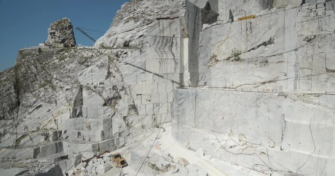 Large white marble quarry with blue sky background.There is a derrick type crane used to lift the large weights of the marble blocks. The cuts of the marble.