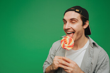 Young man lick lollipop with enjoy, isolated on green background