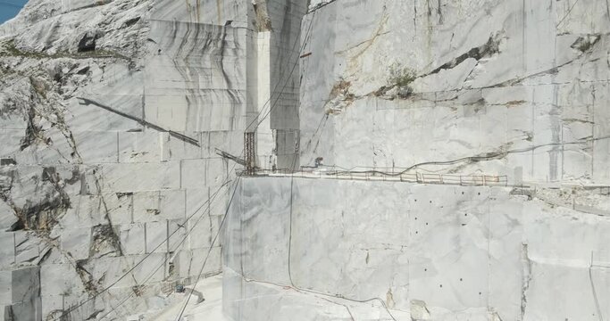 Large white marble quarry with blue sky background.There is a derrick type crane used to lift the large weights of the marble blocks. The cuts of the marble.