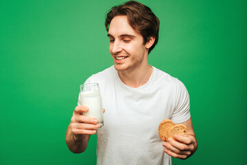 Young man holds glass of milk with cookies, isolated on green background