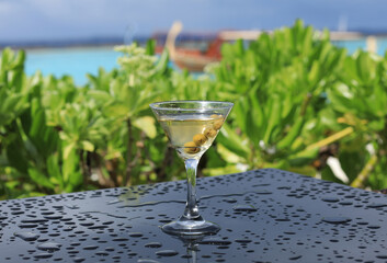 glass with martini cocktail with olives on the table outdoors in summer