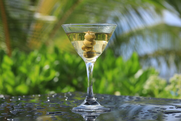 glass with martini cocktail with olives on the table outdoors in summer