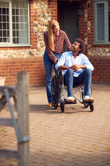 Mature Couple With Man Sitting In Wheelchair Being Pushed By Woman Outside Home