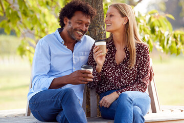 Loving Mature Couple Relaxing Sitting Together On Bench Under Tree In Summer Park With Coffee