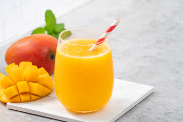 Fresh mango juice smoothie in a glass cup on gray table background.