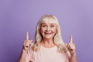 Positive old woman point finger up copy space over purple background