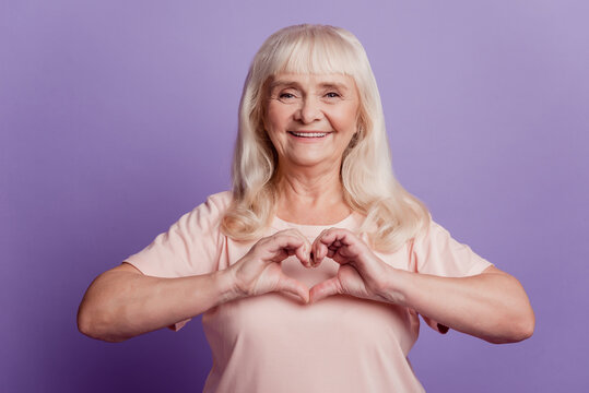 Photo of positive old wpman show heart gesture near chest on violet background