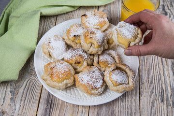 A woman's hand picks up a Portuguese home-baked dessert with egg cream from a plate . Dessert Pasteis de nata.